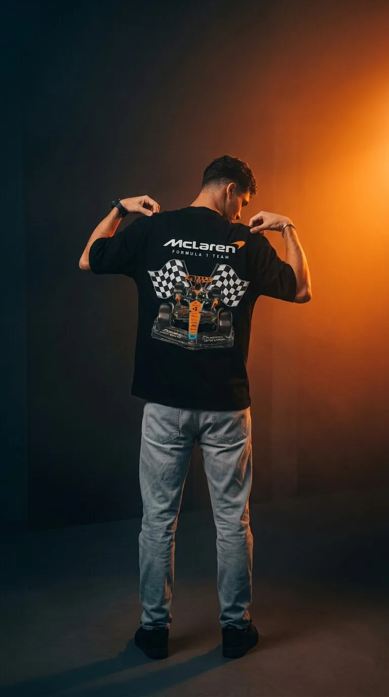 AHS Premium Wear — McLaren Formula 1 oversized graphic tee, back view, shot in a paddock with papaya-orange smoke.